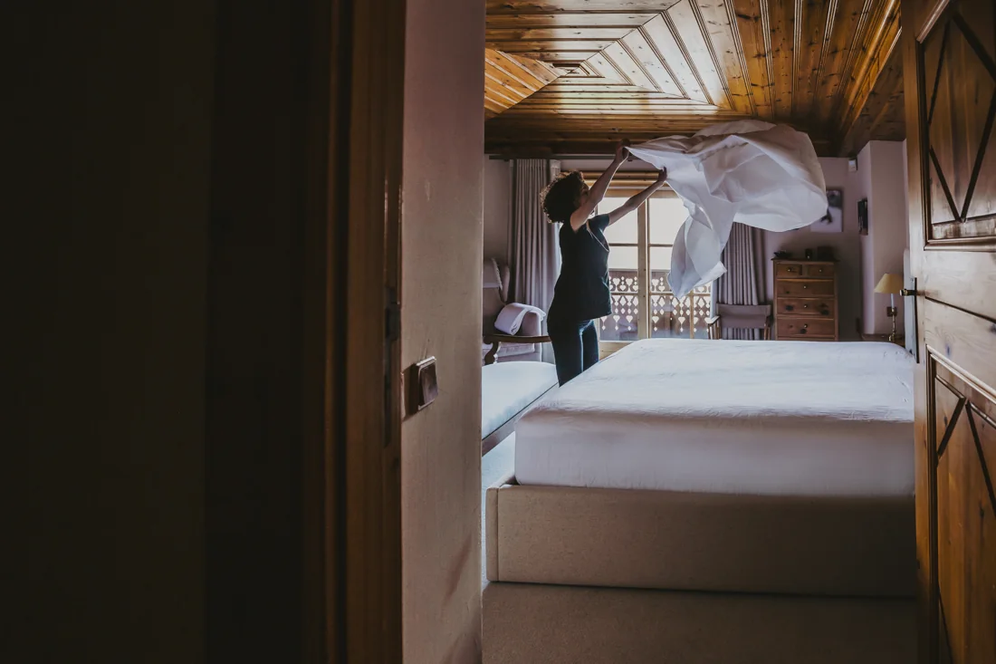An Alpine Shine team member floating fresh linen over a chalet bed